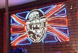A neon sign that says God Save the Queen with a background of the British flag.