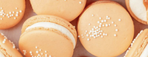 A bunch of macarons in the new 2024 Pantone Color of the Year, Peach Fuzz, with white filling and sugar on top
