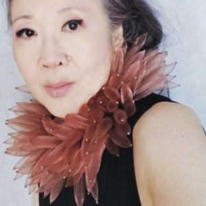 Susan Ishida, Creative Director of Trendspot, wears a mauve feather collar and black shirt. In front of a white background