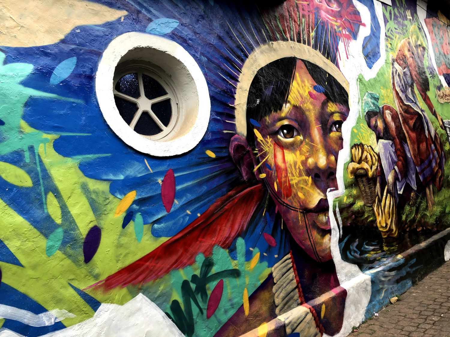 A colorful wall mural in Brazil featuring an indigenous woman in a brightly colored feathered headress.