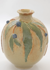 a small tan vase with bay leaves and blue berries