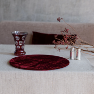 A beige table cloth with burgundy velvet placemat, a burgundy goblet and burgundy berries