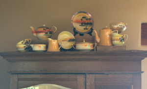 a collection of vintage noritake porcelain in sunset colors painted with a coastline landscape. Displayed on top of an armoire